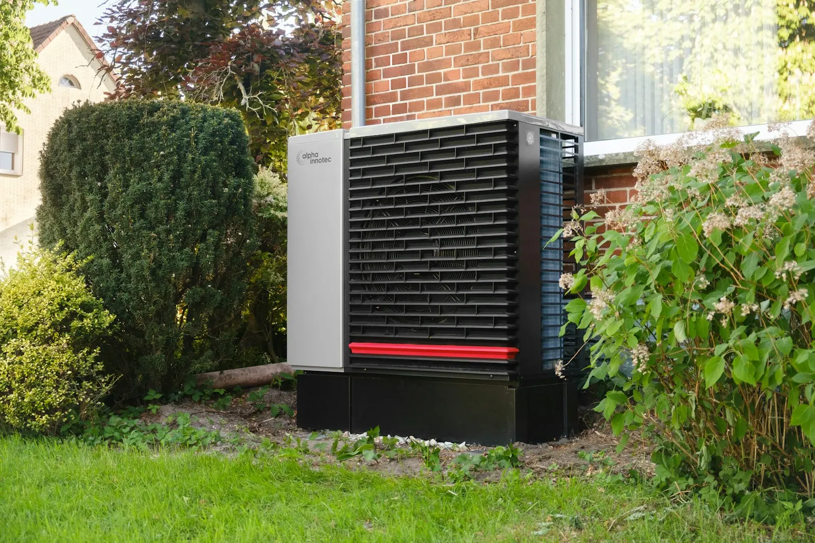 Pompe à chaleur monobloc dans un jardin, contre une maison en briques